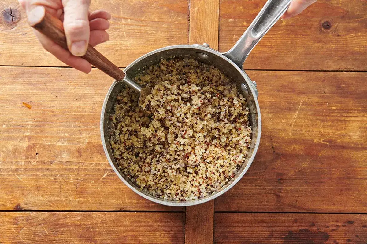 H&auml;nde r&uuml;hren in einem Topf mit gekochtem Quinoa tricolore.