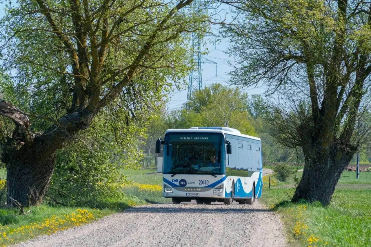 Autobus PKS Słupsk jedzie polną drogą wśród zieleni i żółtych kwiatów. To może być Twój sposób, jak dojechać do Jarosławca autobusem.