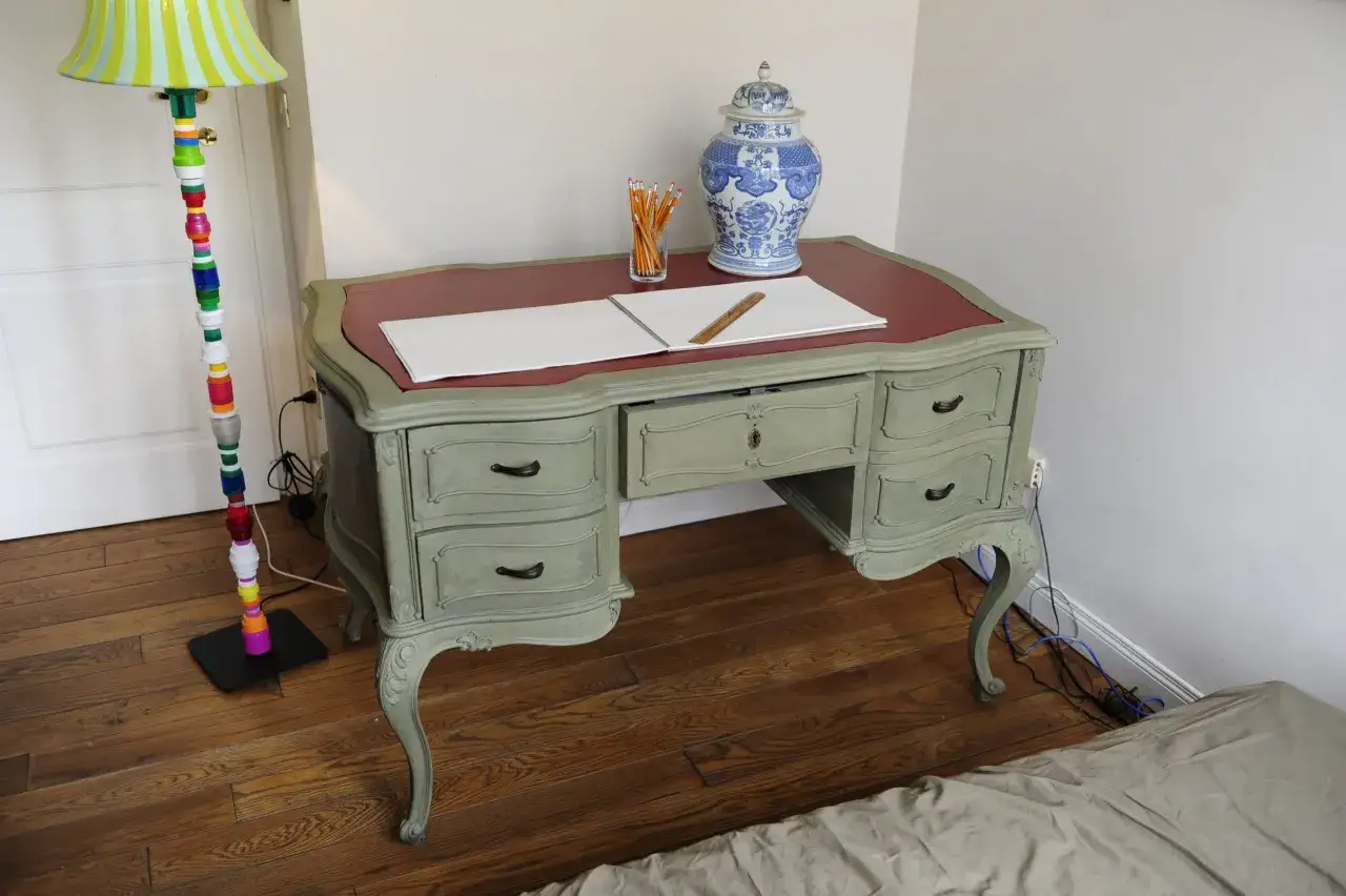 Scrivania in stile shabby chic, con piano in pelle rossa, decorata con un vaso blu e bianco e matite. Un progetto di pittura shabby fai da te che dona un tocco di classe.
