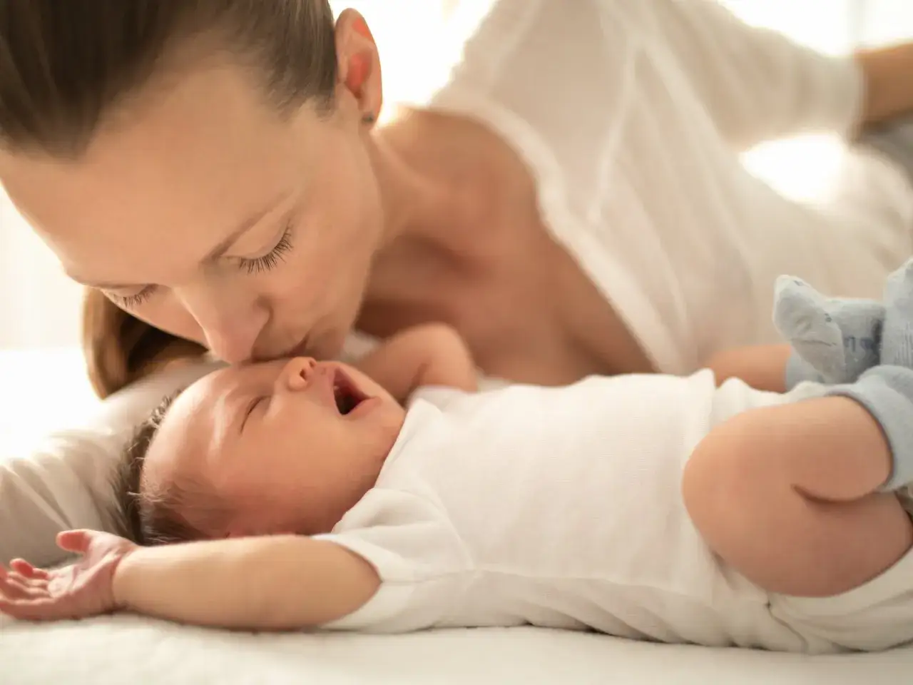 Mutter küsst ihr Baby auf die Stirn. Das kleine Kind kommt jede Nacht ins Elternbett, um Trost und Nähe zu finden.
