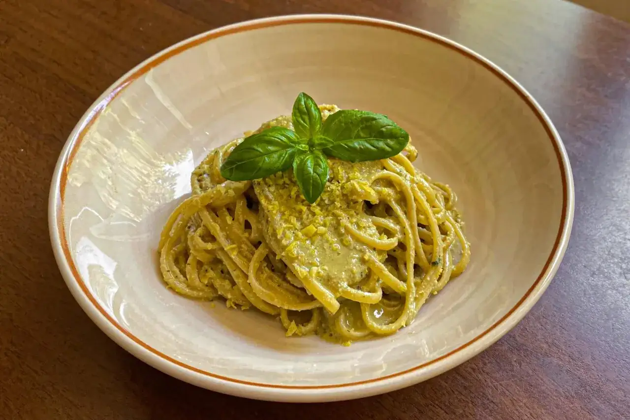 Spaghetti conditi con un cremoso pesto al limone, guarniti con basilico fresco e scorzetta di limone.