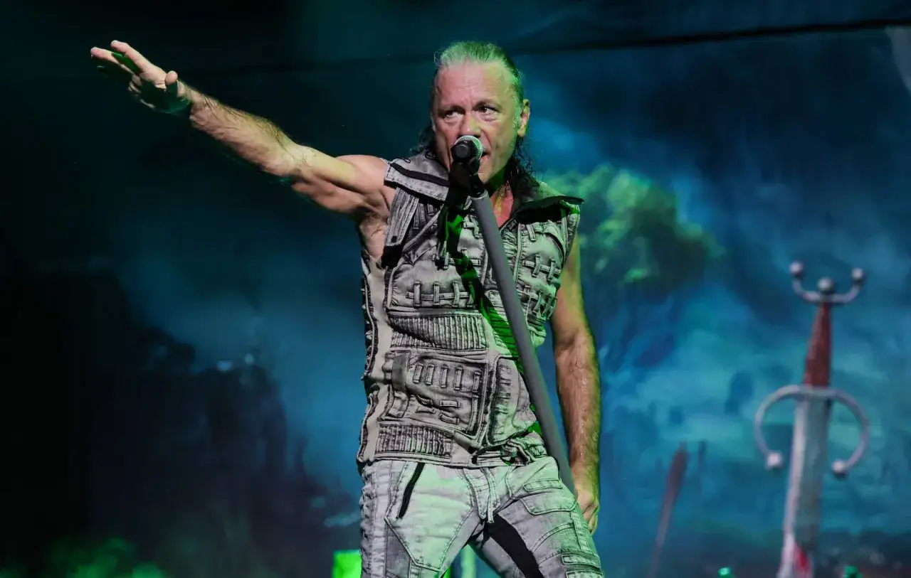 Bruce Dickinson, wokalista Iron Maiden, w swoim charakterystycznym stylu na scenie, z uniesioną ręką i mikrofonem.