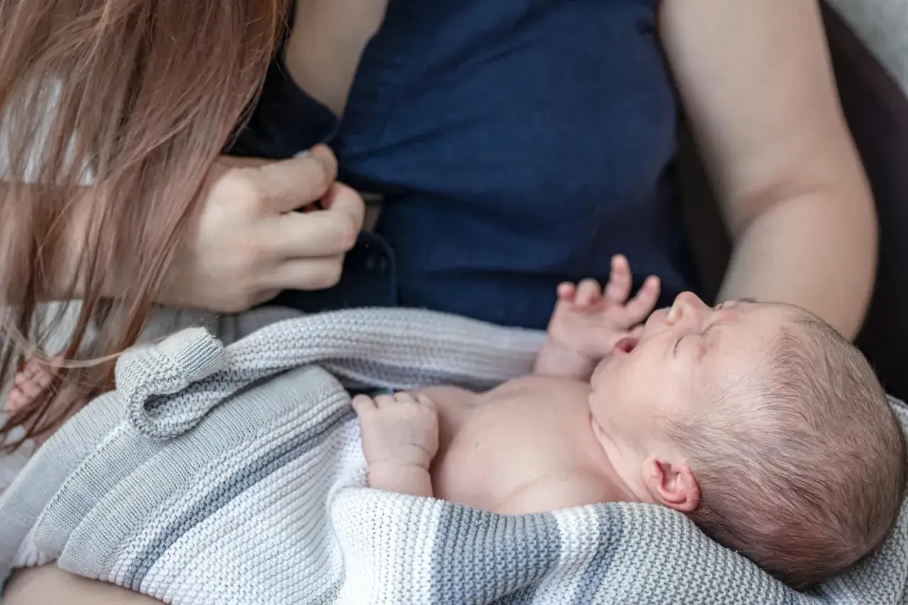 Mama tuli do piersi, kiedy zanika pokarm. Dziecko płacze, otulone kocykiem.