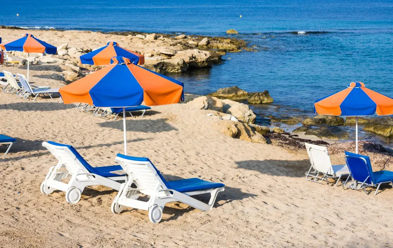 Plaża na Cyprze w październiku. Leżaki i parasole czekają na plażowiczów. Słoneczna pogoda sprzyja relaksowi nad morzem.