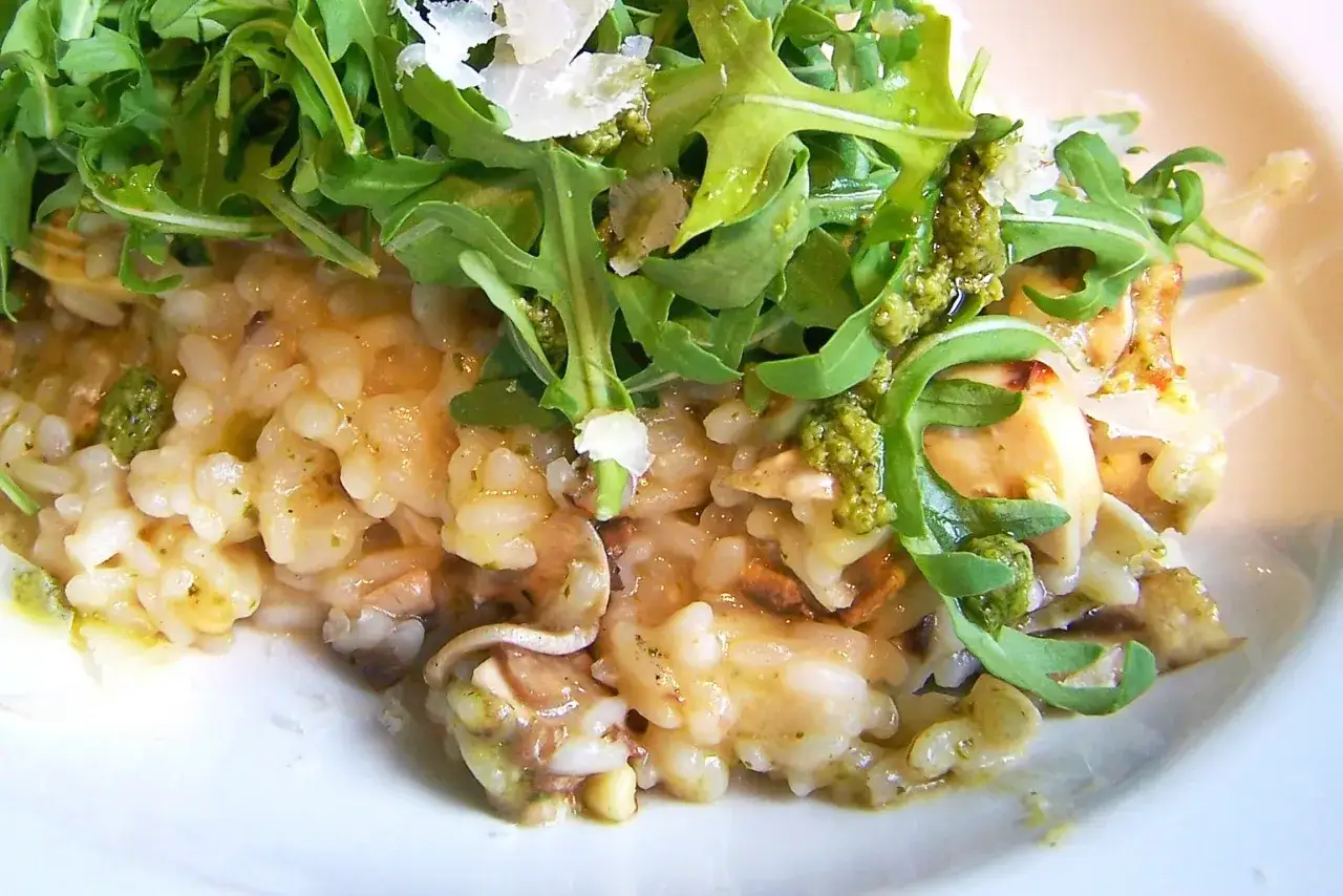 Kremowe risotto z pieczarkami, polane zielonym pesto i posypane parmezanem, podane z rukolą.