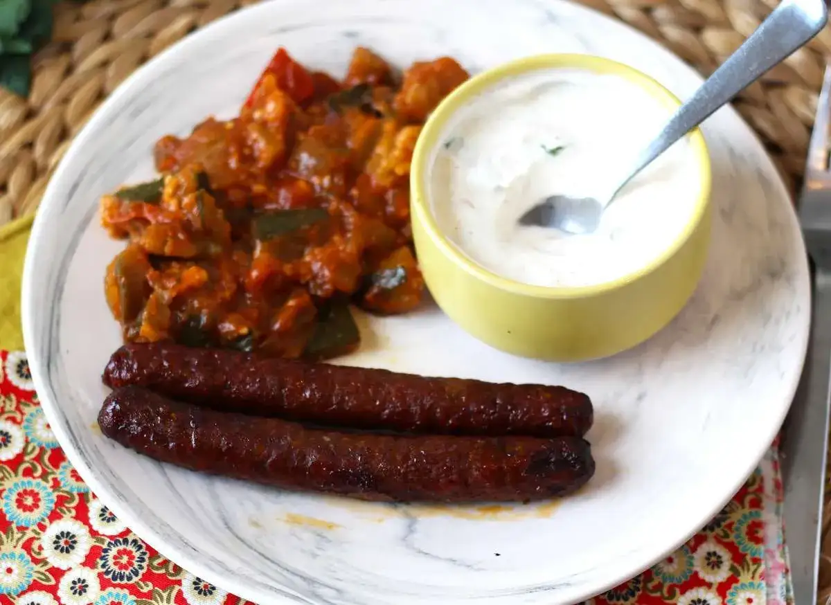 Dos salchichas merguez, picante guiso de verduras y una salsa cremosa en un plato.