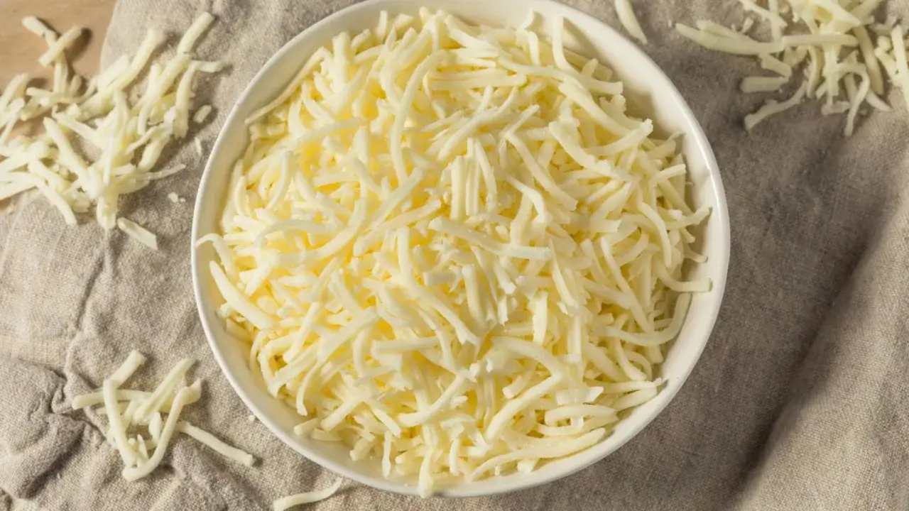 Un bol blanco lleno de queso mozzarella rallado, la mejor mozzarella para pizza, sobre una tela rústica.