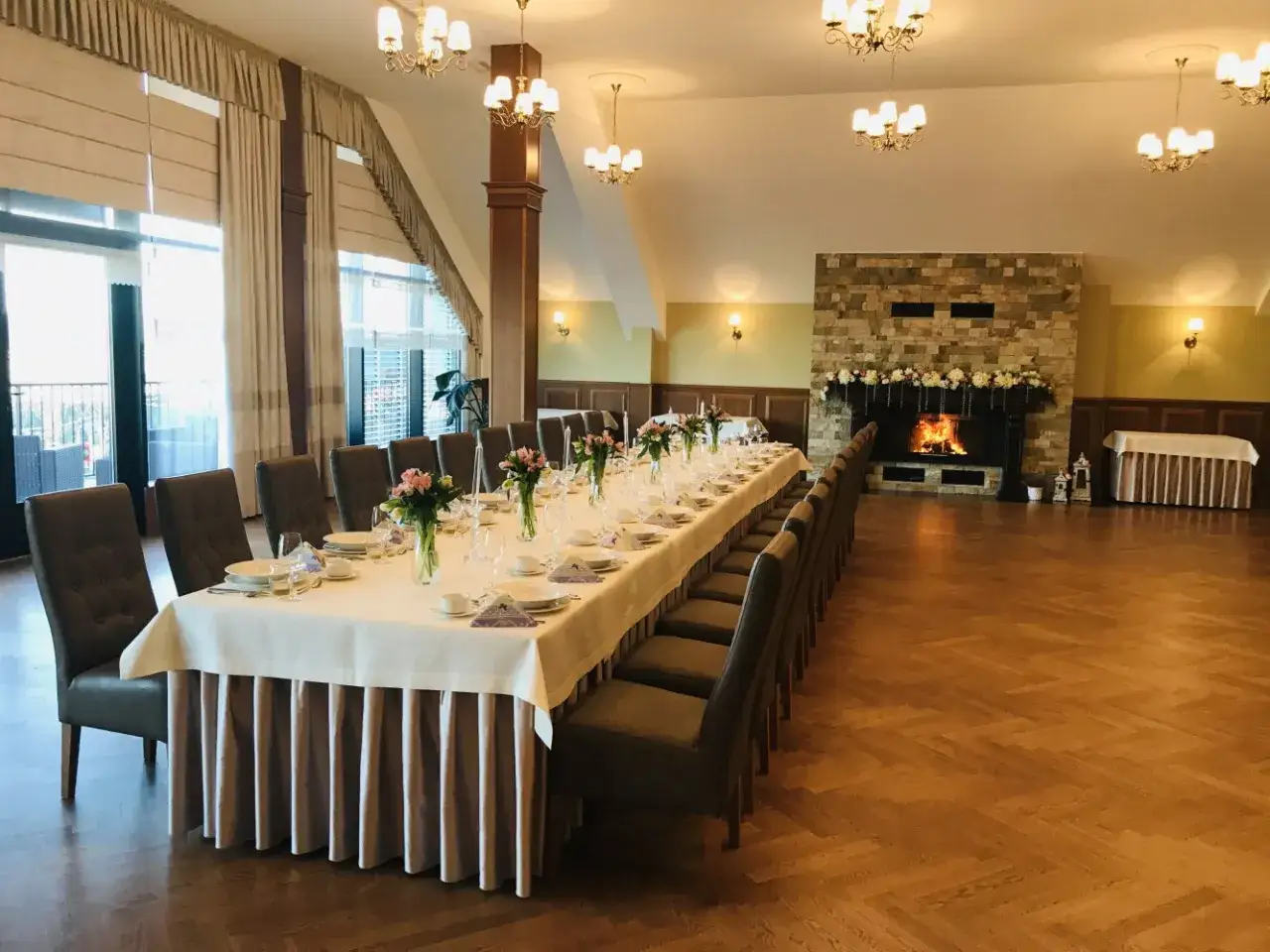 Elegancka sala bankietowa ośrodka jeździeckiego Lando z długim stołem nakrytym na uroczystość, kominkiem i stylowymi żyrandolami.