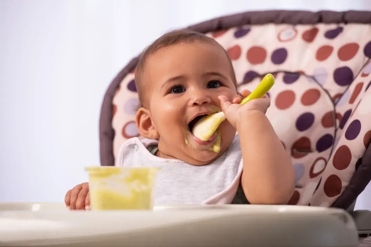 Bebé feliz probando su primer pure para bebes con una cuchara verde.