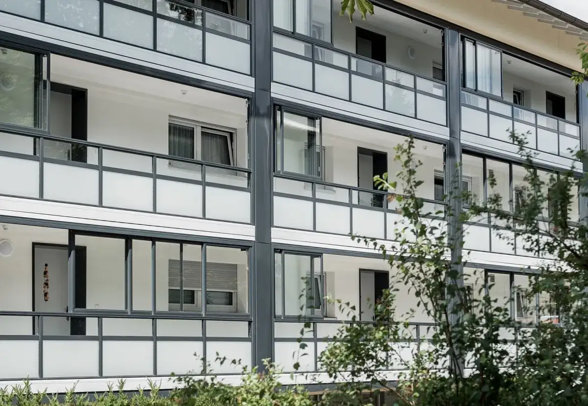 Moderne Wohnanlage mit Balkonen und großen Fenstern. Der notwendiger flur ist hier durch die durchgehenden Glasfronten gut beleuchtet.