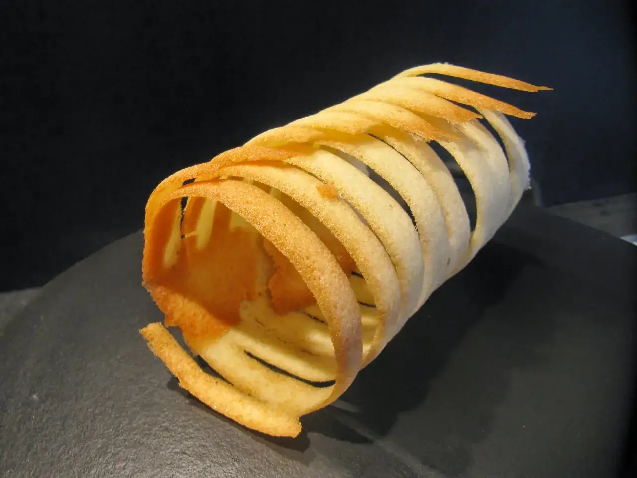 Un rouleau de pâte à cigarette, fin et doré, forme une spirale aérienne sur un fond sombre.