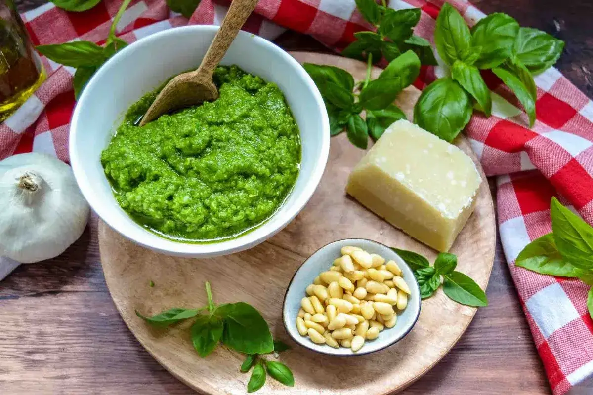 Frisches Pesto in einer Schüssel, daneben Pinienkerne, Parmesan, Knoblauch und Basilikum. Perfekt für leckere Pesto Rezepte.