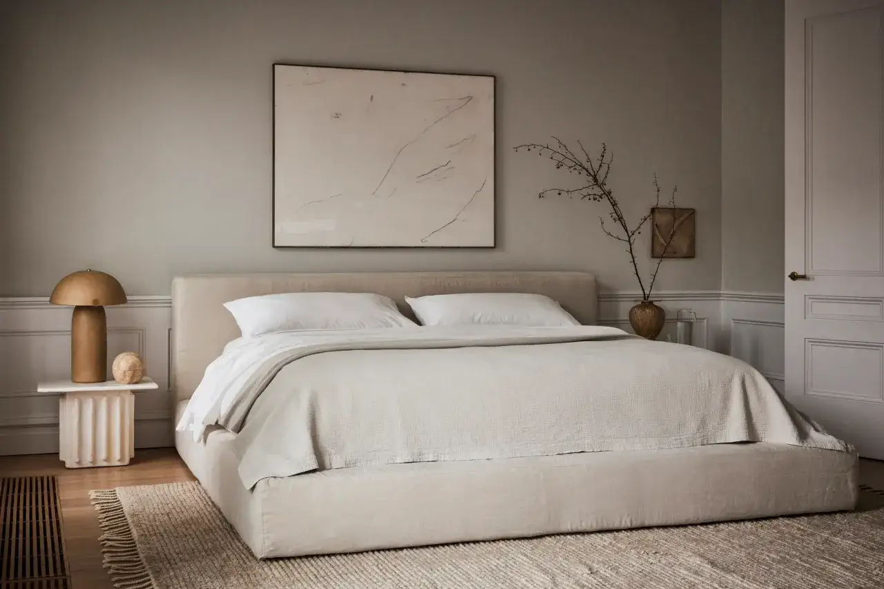 Une chambre beige paisible avec un grand lit, une table de chevet design et une &oelig;uvre d'art abstraite.
