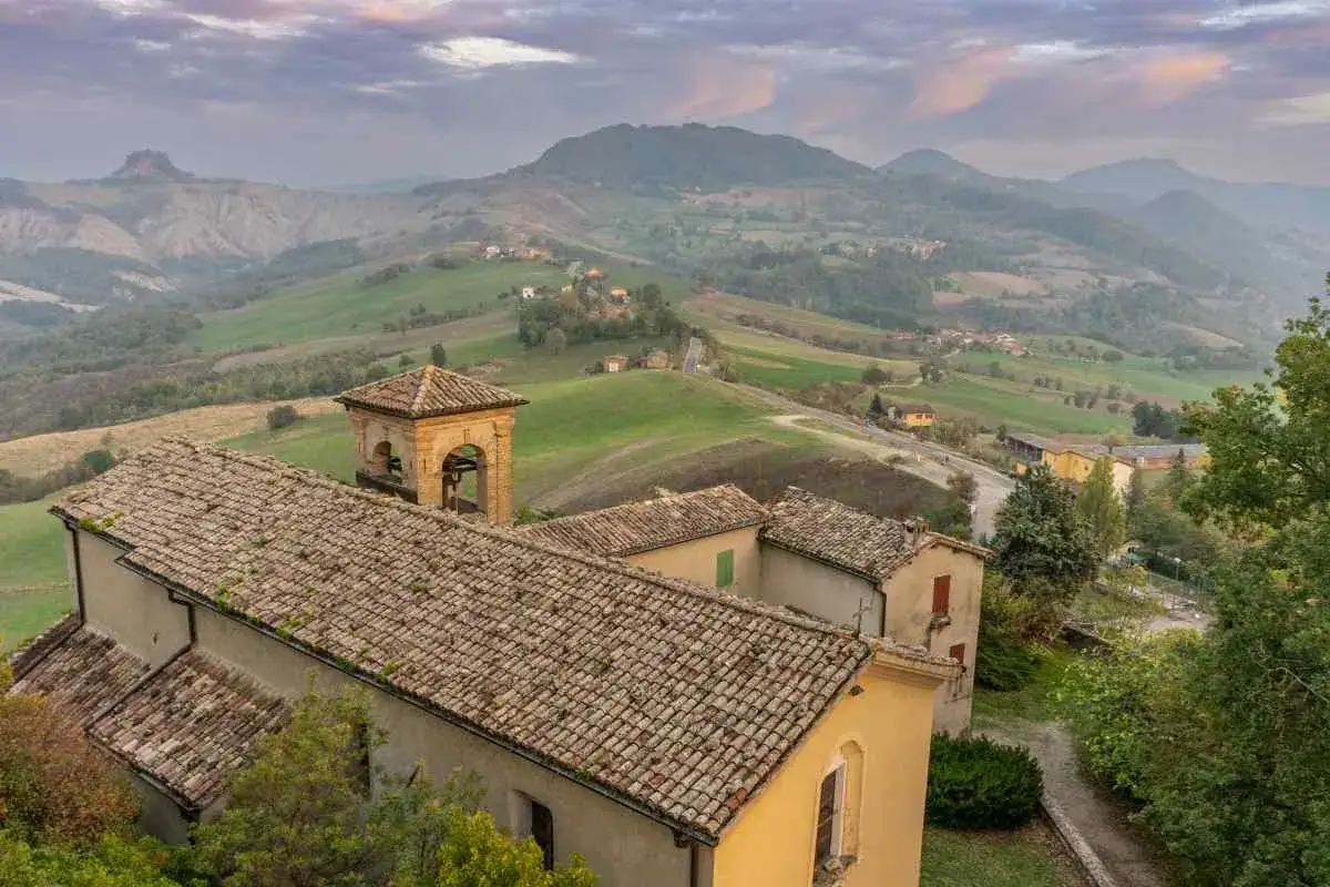 Borghi collinari perfetti per gite in giornata da Reggio Emilia. Un campanile svetta tra tetti antichi e dolci pendii verdi.