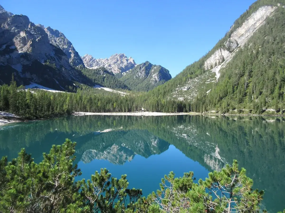 Spiegelglatter Bergsee mit Fichtenwäldern und felsigen Gipfeln, ein Traumziel auf der Alta Via 1.