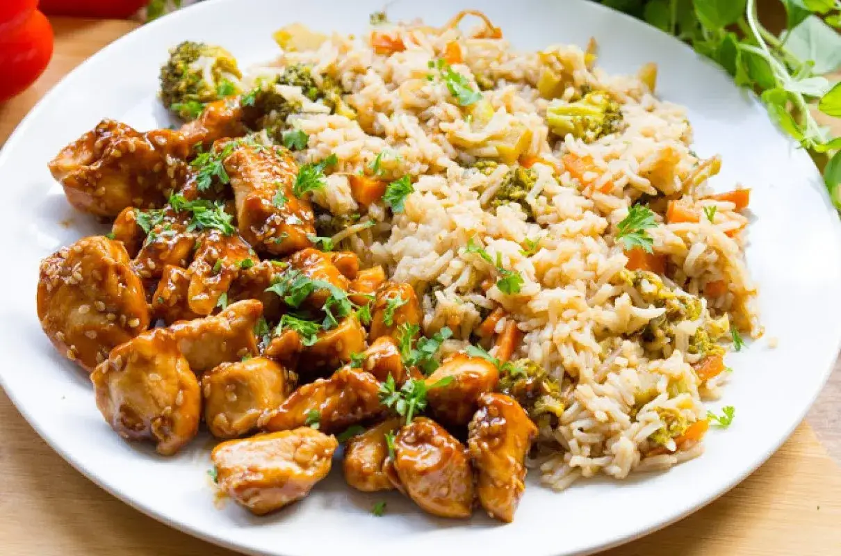 Kurczak w marynacie teriyaki z ryżem i warzywami. Danie posypane sezamem i natką pietruszki.
