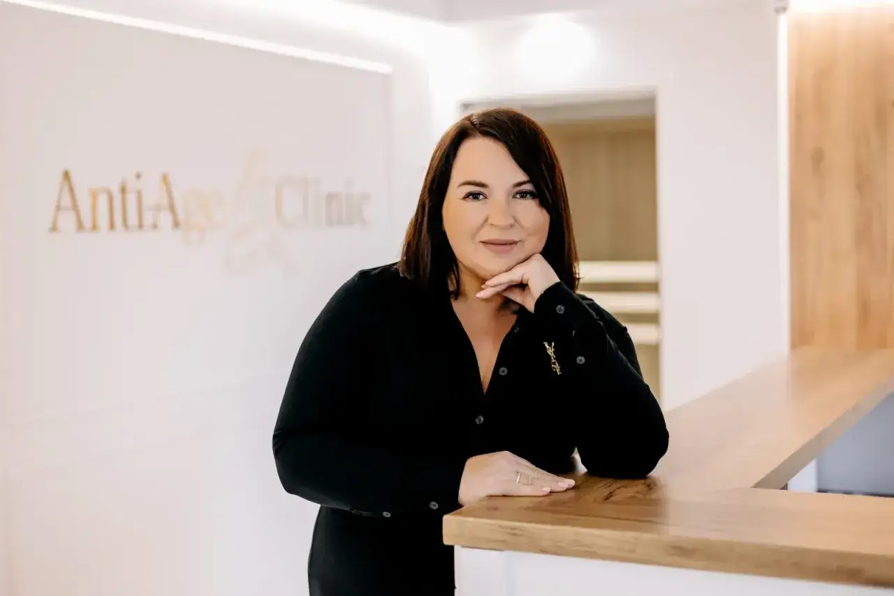 Kobieta w czarnej bluzce opiera się o ladę w klinice AntiAge Clinic.