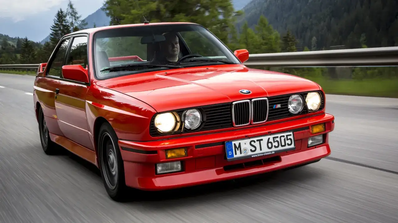 Czerwone BMW E30 M3, ikona wśród **bmw modele stare**, pędzi malowniczą drogą w górach.