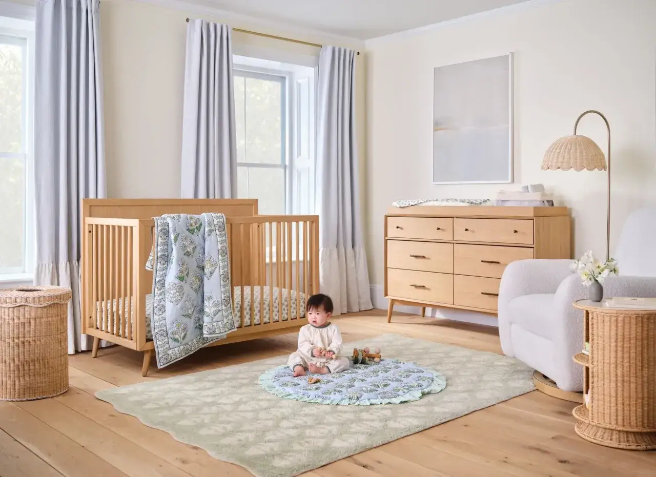 A serene baby room inspiration with a wooden crib, changing dresser, and a baby sitting on a playmat.