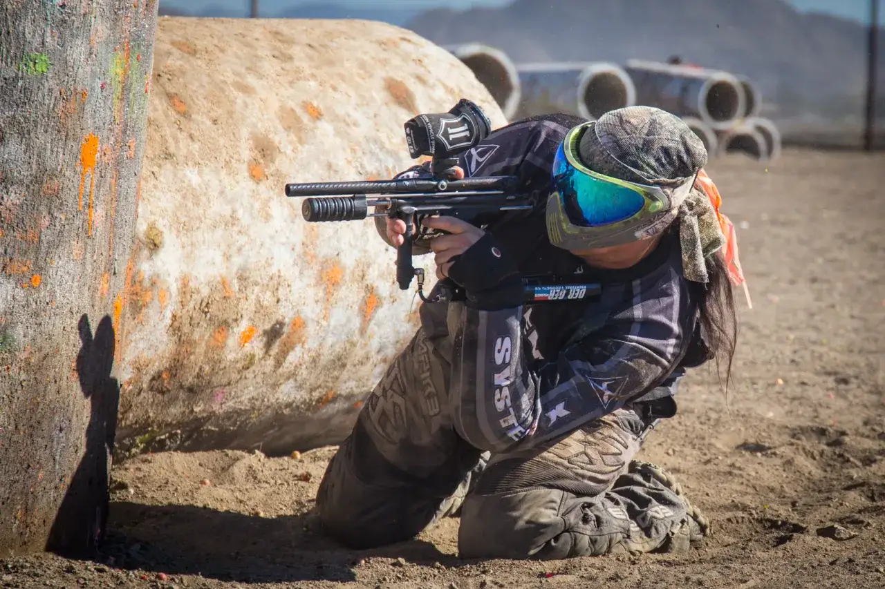 Jugador de paintball agachado, listo para disparar. El paintball vs airsoft es una batalla de estrategia y adrenalina.