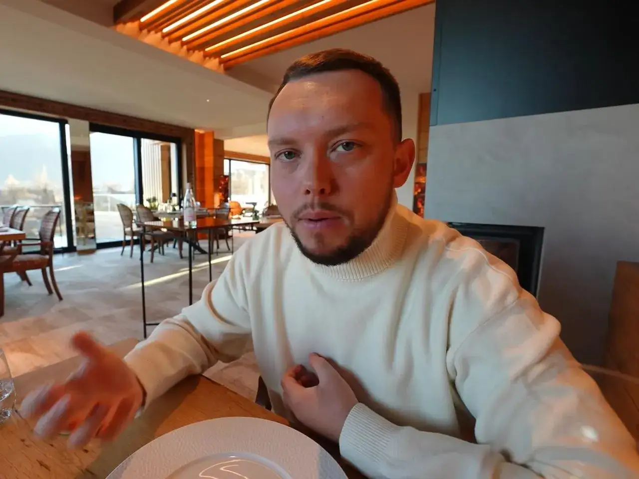 Książulo w eleganckiej restauracji, gdzie jego recenzja obiadu była negatywna. Widać wnętrze z dużymi oknami i stołami.