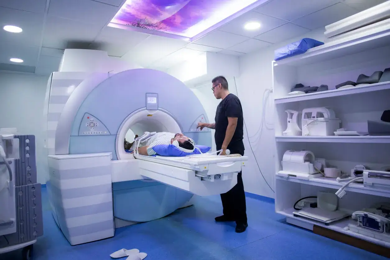Pacjent leży w aparacie do rezonansu magnetycznego, przygotowując się do badania. Technik kontroluje proces, zapewniając komfort pacjenta podczas rezonansu jamy brzusznej.