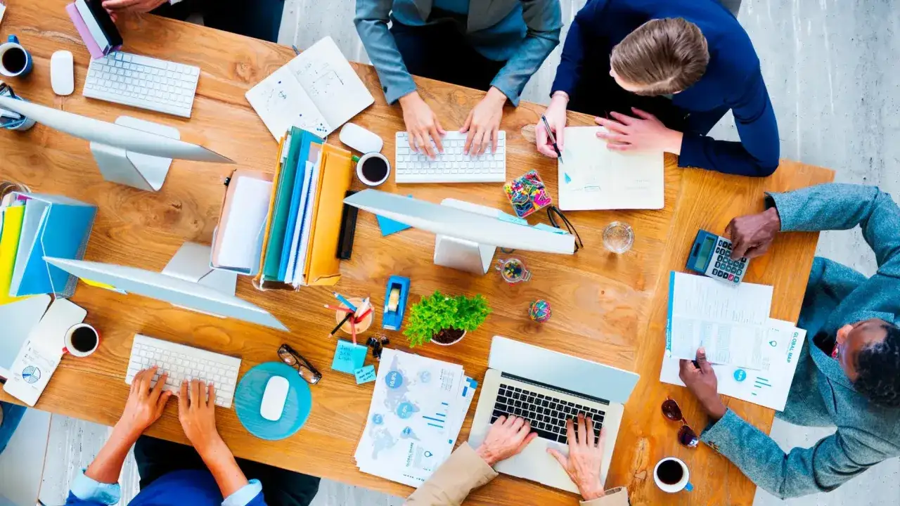 J&oacute;venes colaborando en ideas de negocios, con laptops, papeles y tazas de caf&eacute; sobre una mesa de madera.