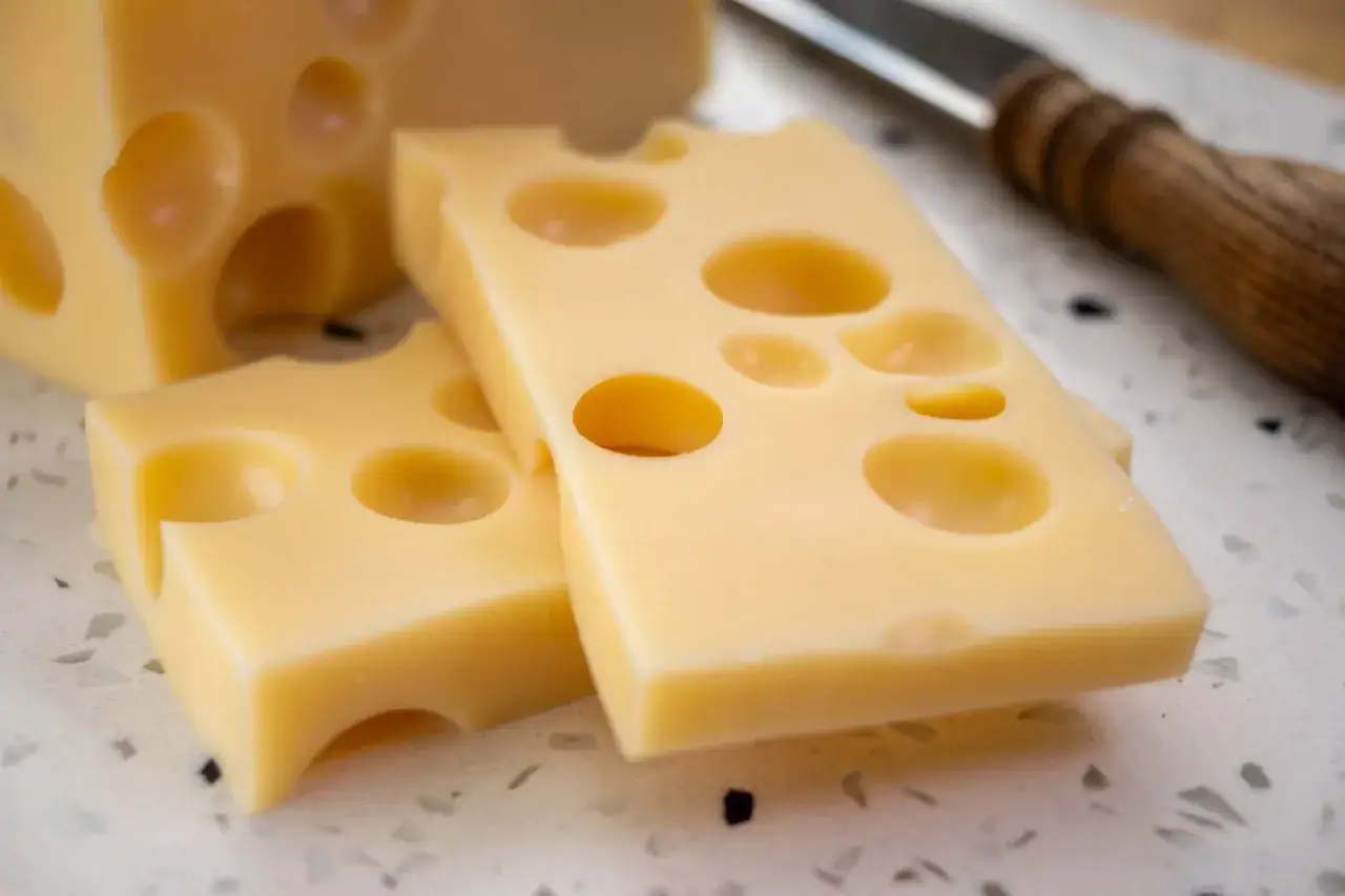 Fette di formaggio con i buchi, pronte per essere gustate. Un coltello con manico in legno sullo sfondo.