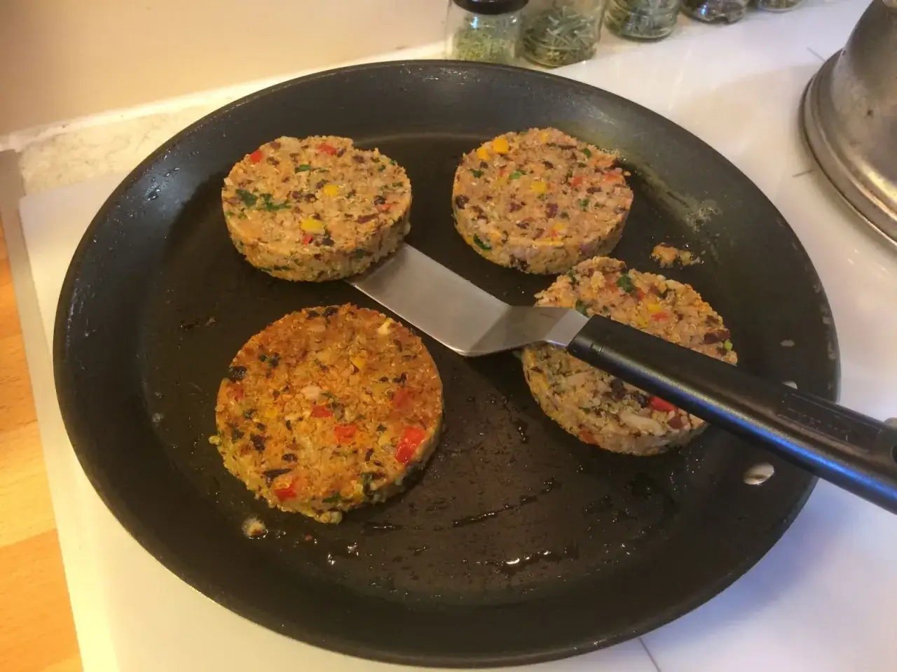 Quatre galettes de haricot rouge, color&eacute;es et garnies de l&eacute;gumes, dorent dans une po&ecirc;le avec une spatule.