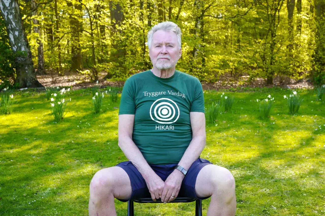 &Auml;ldre man sitter i en gr&ouml;nskande park, med en t-shirt som s&auml;ger 