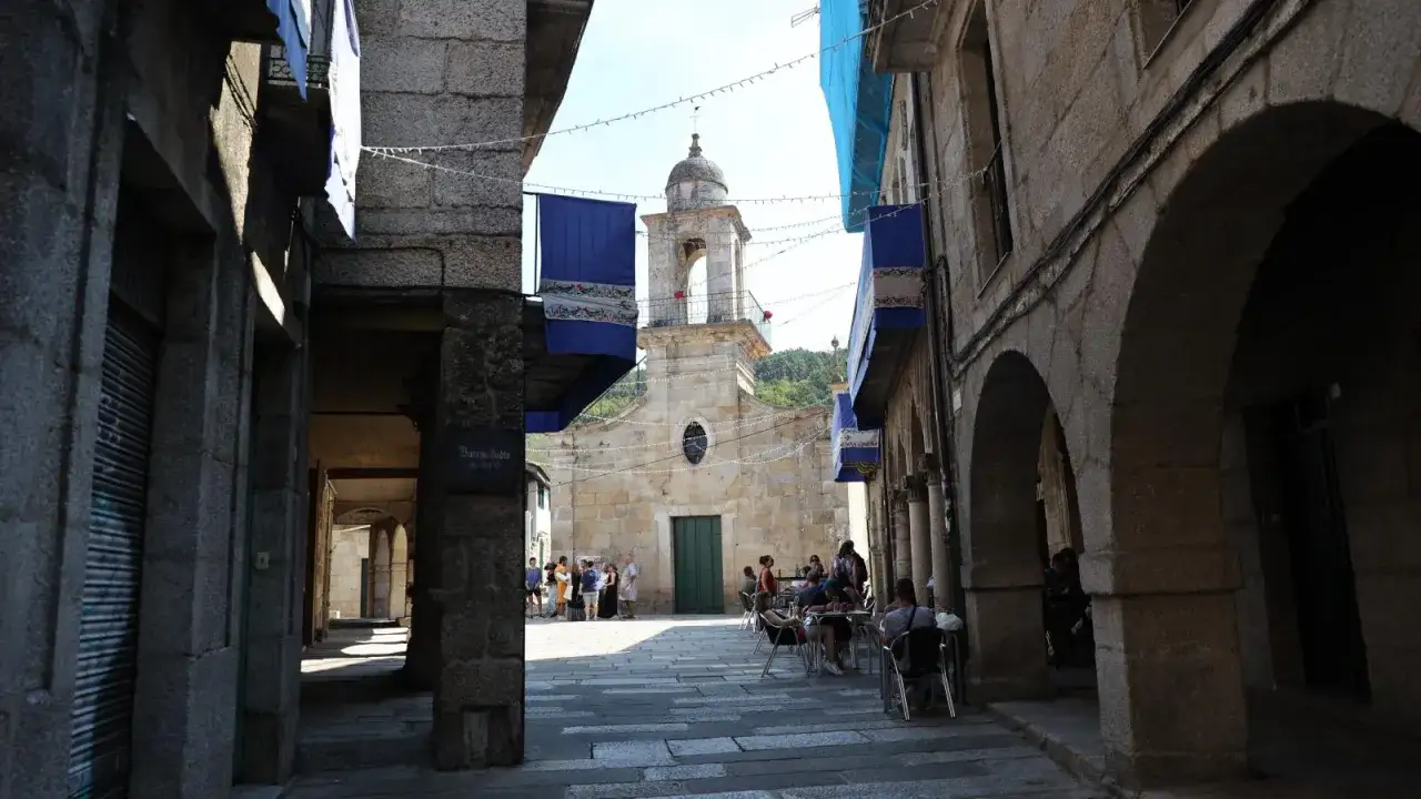 Plaza con iglesia y gente disfrutando en terrazas. Un lugar encantador que ver en Ribadavia, con su arquitectura histórica y ambiente acogedor.