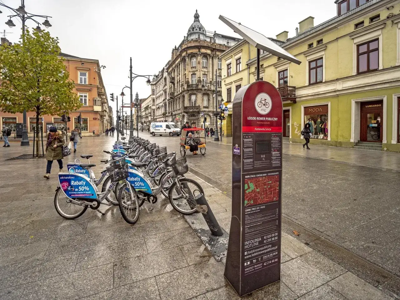 Rowerowy Łódź: rząd rowerów miejskich czeka na chętnych do odkrywania tras rowerowych Łodzi. Stacja z panelem informacyjnym.
