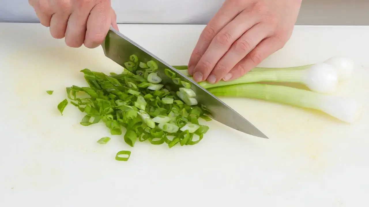 H&auml;nde schneiden Lauchzwiebeln f&uuml;r das Einfrieren. Frische gr&uuml;ne Zwiebeln werden auf einem Schneidebrett zerkleinert.