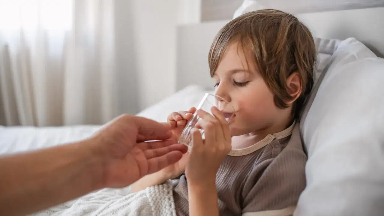 Chory chłopiec pije wodę z szklanki, opiekun podaje mu ją. Objawy salmonella u dzieci mogą być łagodne, ale ważne jest nawodnienie.