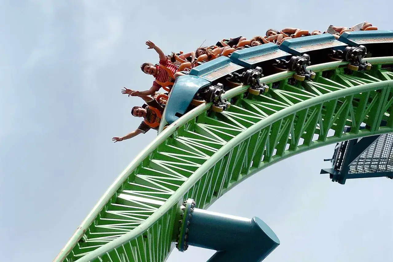 Ludzie krzyczą z radości, zjeżdżając z **najwyższego rollercoastera na świecie**. Zielona konstrukcja wznosi się ku niebu.