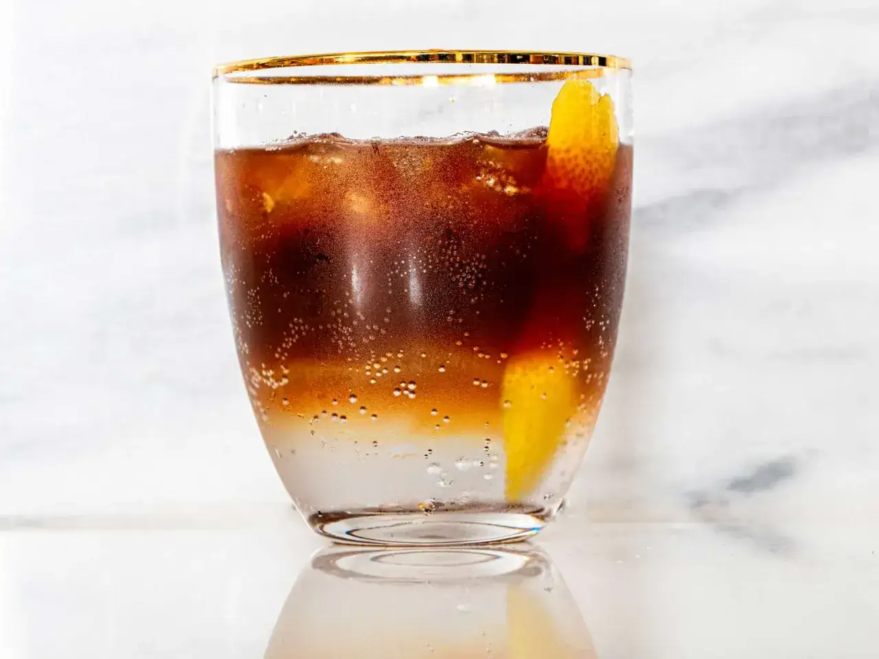 Orzeźwiający tonic espresso z lodem i skórką cytryny, w szklance ze złotym rantem.
