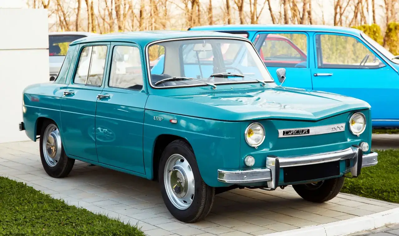 Turkusowa Dacia 1100, której kraj pochodzenia to Rumunia, stoi na chodniku.