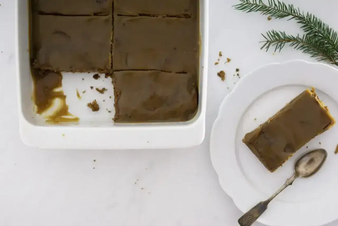 En bit av en h&auml;rlig sticky toffee pudding i en vit form, en annan bit ligger p&aring; en tallrik med en sked.
