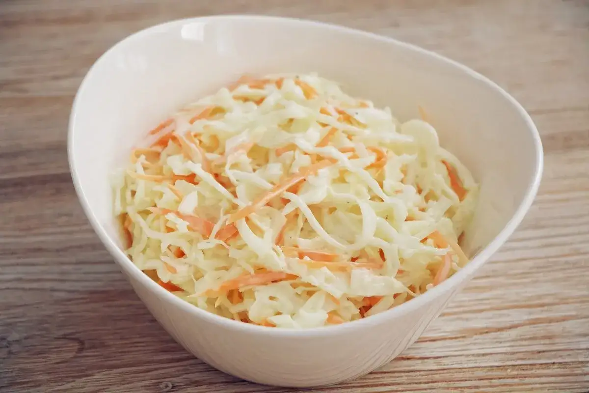 Un taz&oacute;n blanco lleno de ensalada de col cremosa, con finas hebras de zanahoria anaranjada mezcladas con la col rallada.