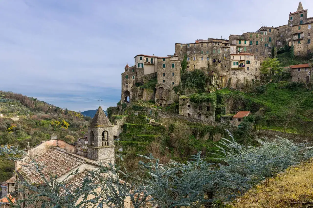 Borgo ligure arroccato su una collina, ideale per strade panoramiche Liguria in moto. Chiesa con campanile in primo piano.