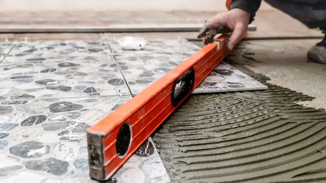 A tiler uses a level to check how to level floor tiles. The patterned tiles are being laid on wet adhesive.