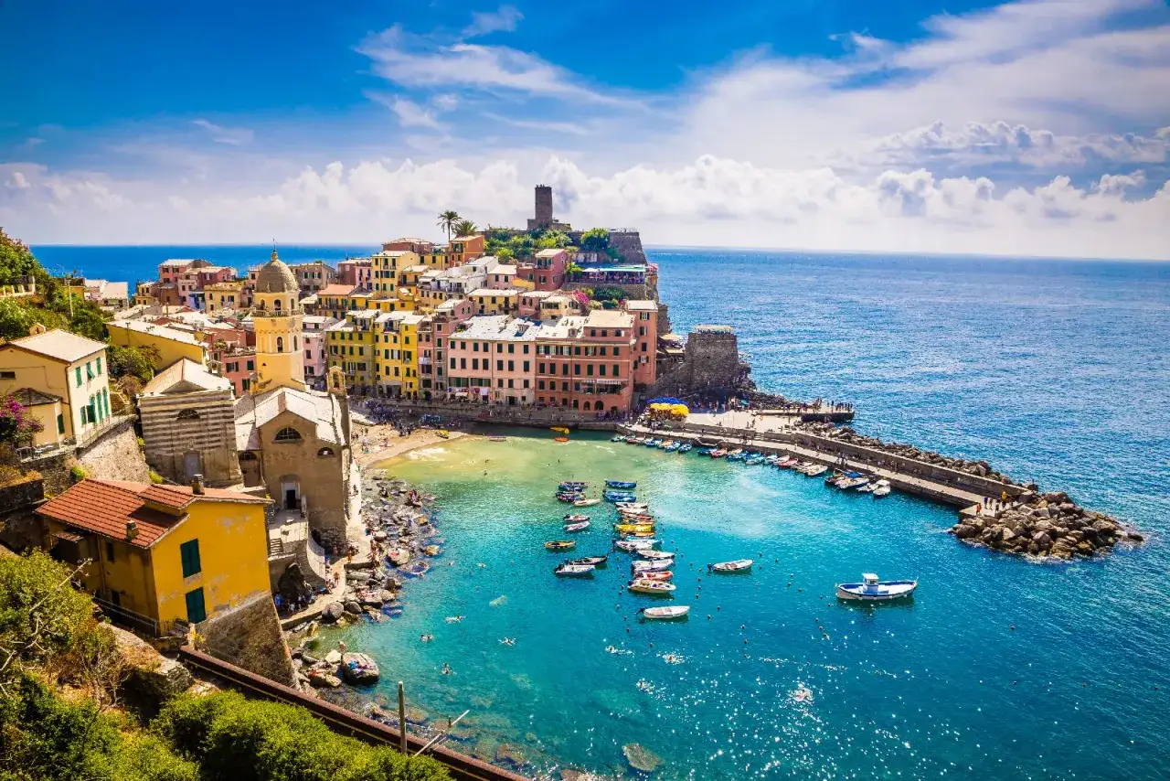 Le Cinque Terre, con le loro case colorate a picco sul mare blu, un porto pieno di barche e un'antica torre di guardia.