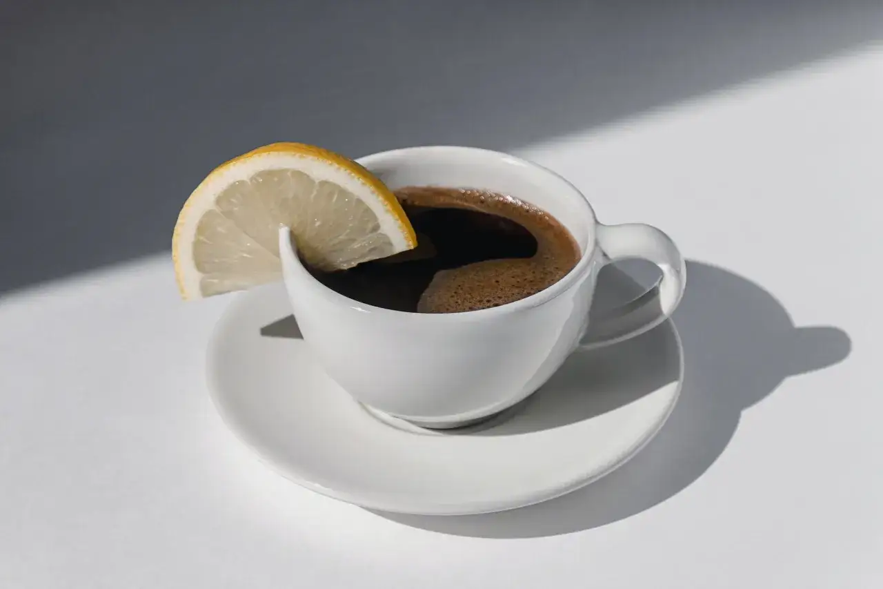 Ein starker Espresso mit Zitrone, eine italienische Spezialit&auml;t, ruht auf einer wei&szlig;en Untertasse.