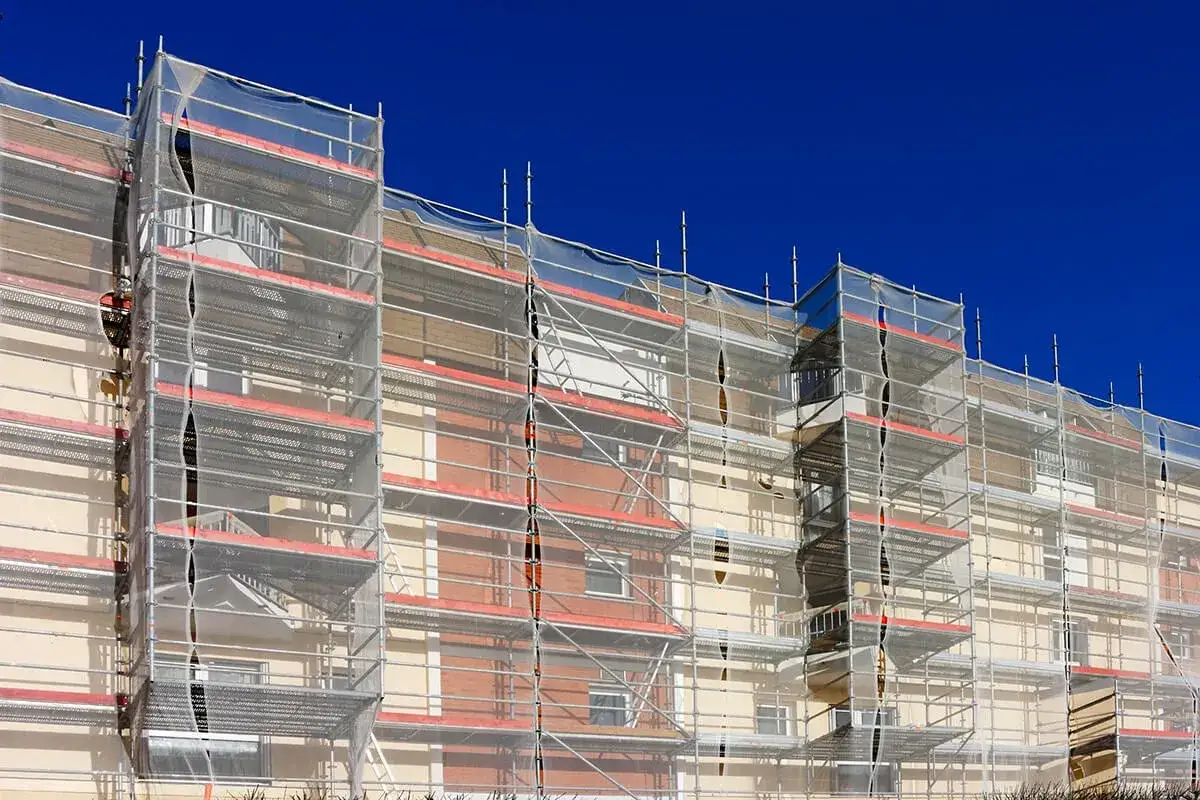 Un immeuble en cours de rénovation, entièrement entouré d'échafaudages et bâché. La peinture de façade sera bientôt terminée.