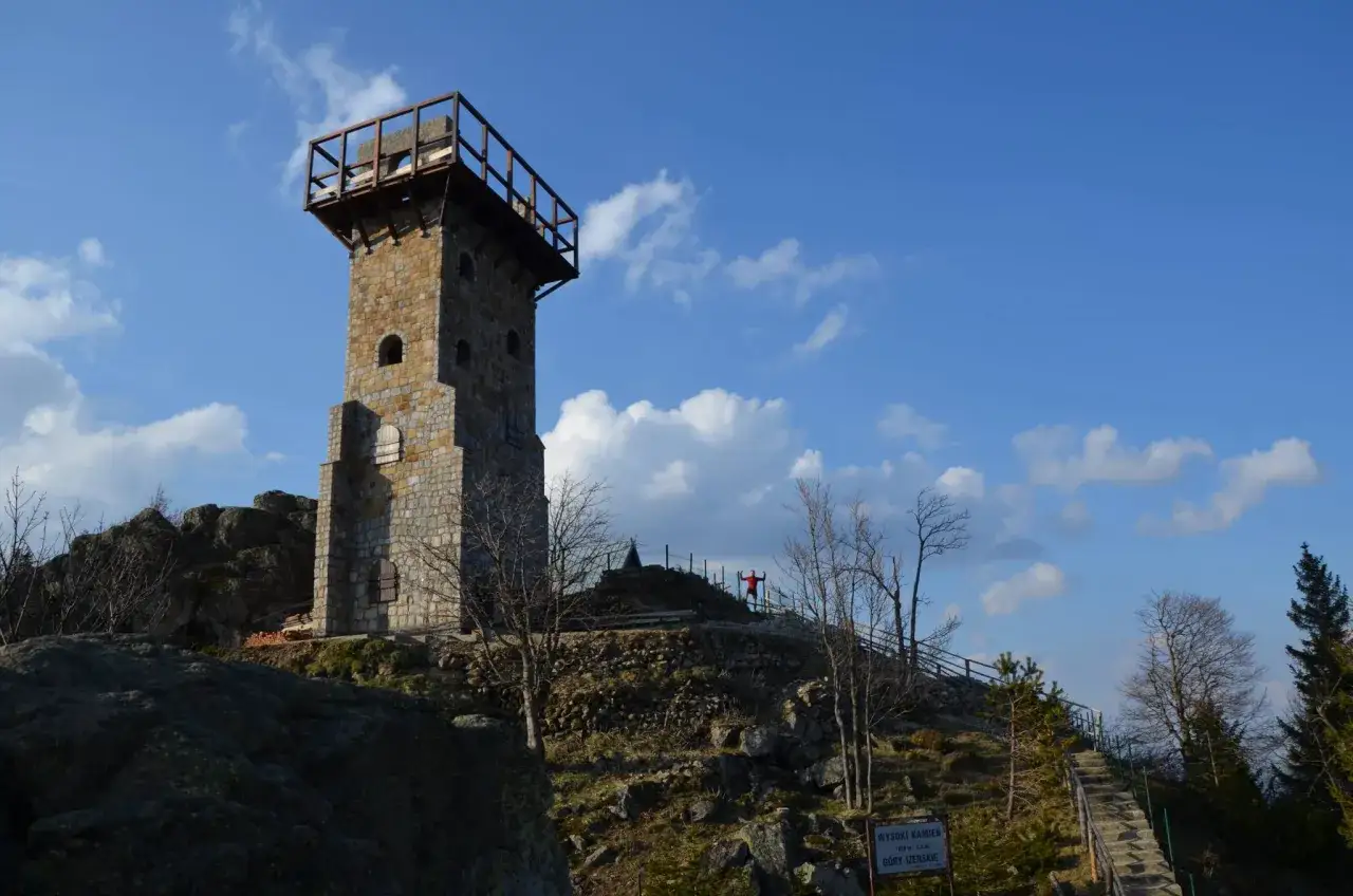Wysoki kamień, wieża widokowa na szczycie góry, z platformą na górze. Na tle błękitnego nieba z chmurami.
