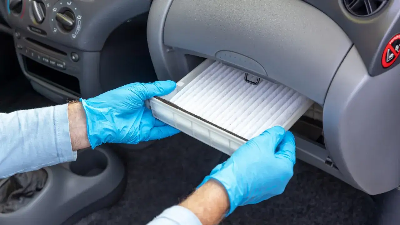 Hands in blue gloves remove a new cabin air filter from its housing, demonstrating how to change cabin air filter for cleaner car air.