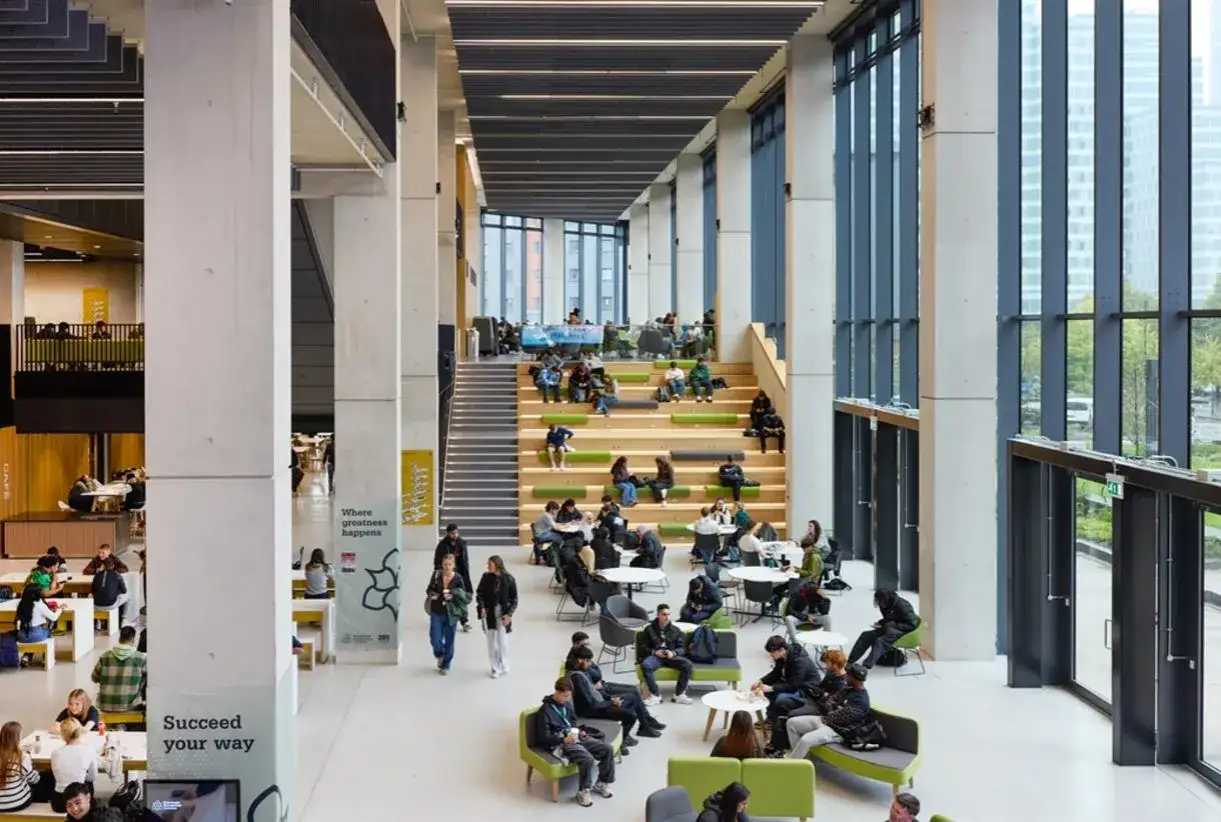 L'université métropolitaine de Manchester, un espace moderne et lumineux où les étudiants se détendent et étudient sur des gradins verts et des tables.
