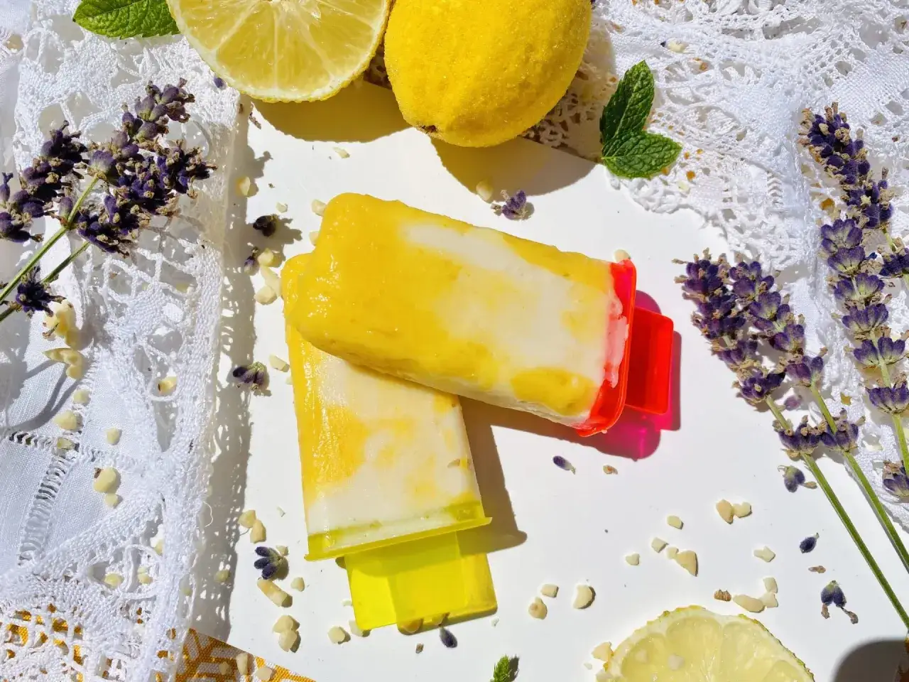 Zwei erfrischende zitronen joghurt eis am Stiel, umgeben von frischen Zitronen, Minze und Lavendel.