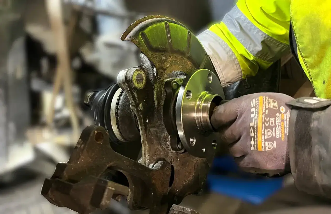 Mechanik w rękawicy montuje nowe łożysko w kole tylnym samochodu.