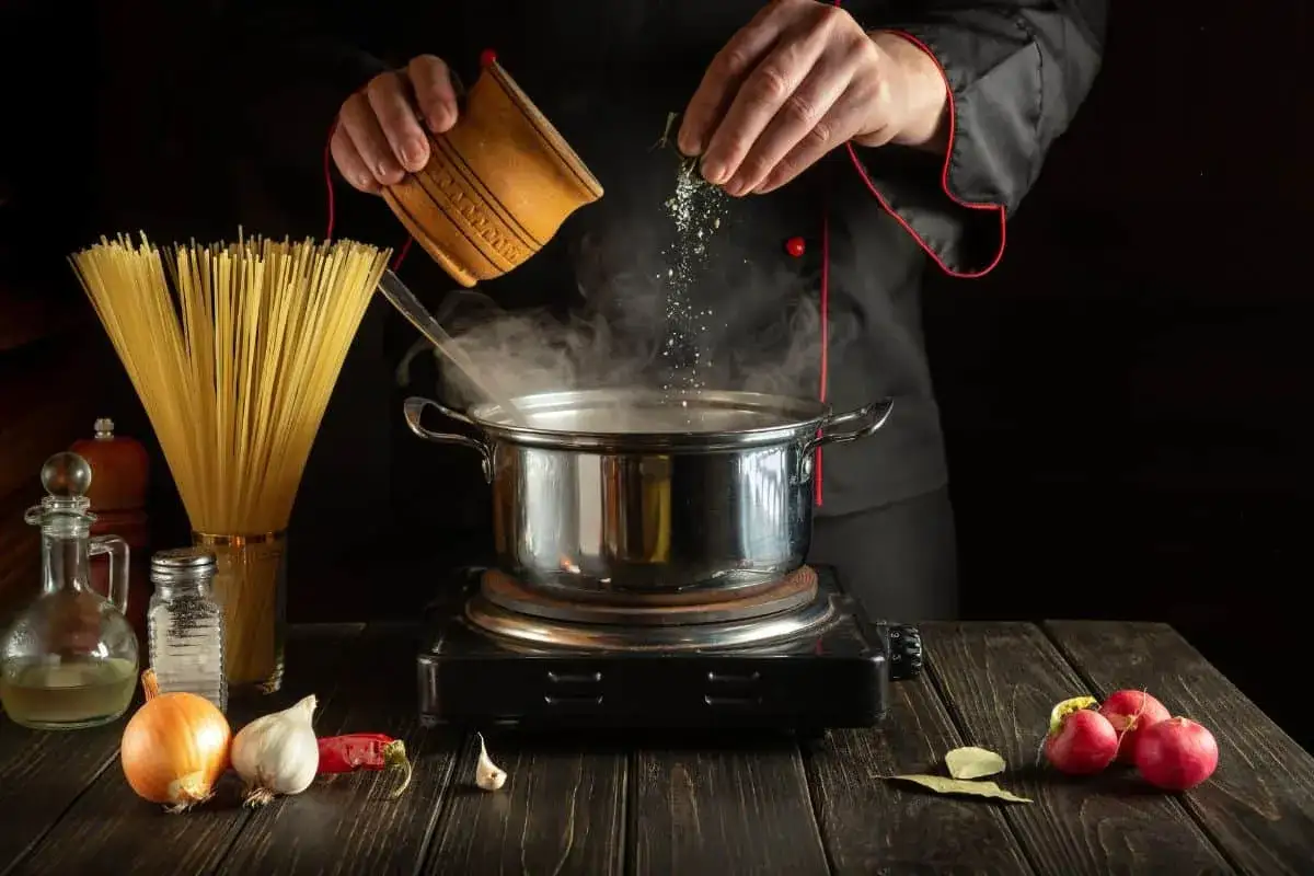 Chef aggiunge quanto sale nella pasta, con spaghetti, cipolla, aglio e ravanelli pronti per la cottura.